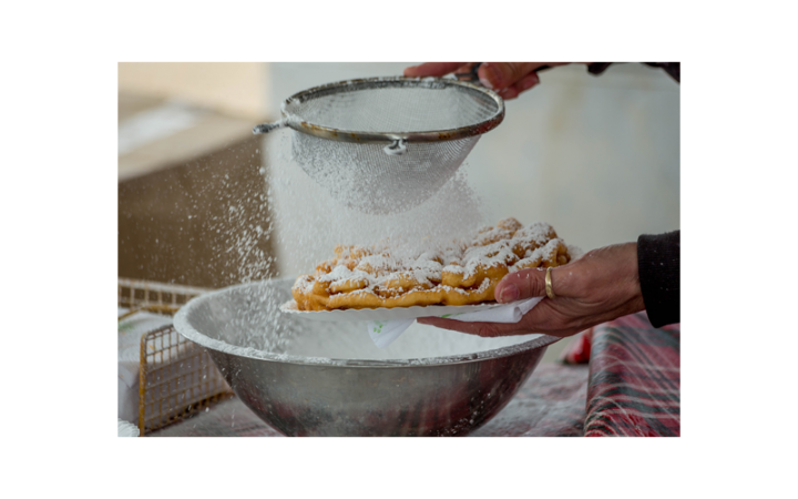 Person's hands sifting powdered sugar onto a funnel cake