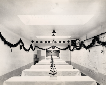 A prisoner mess hall decorated for Christmas with garland and a small tree