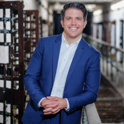 Damon McCool smiles at the camera while leaning on a railing in one of the cellblocks of Eastern State Penitentiary.