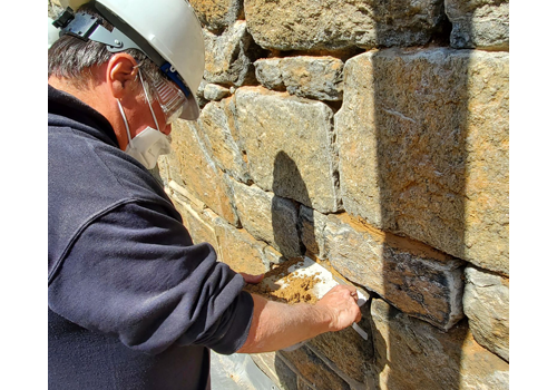 person in a hard hat putting mortar into a stone wall