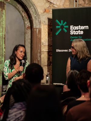 two women sit on a stage with microphones having a conversation