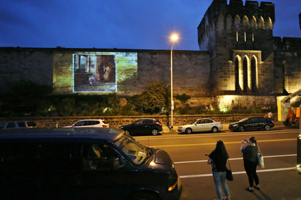 Two people watch as an abstract image is projected onto Eastern State's facade at night