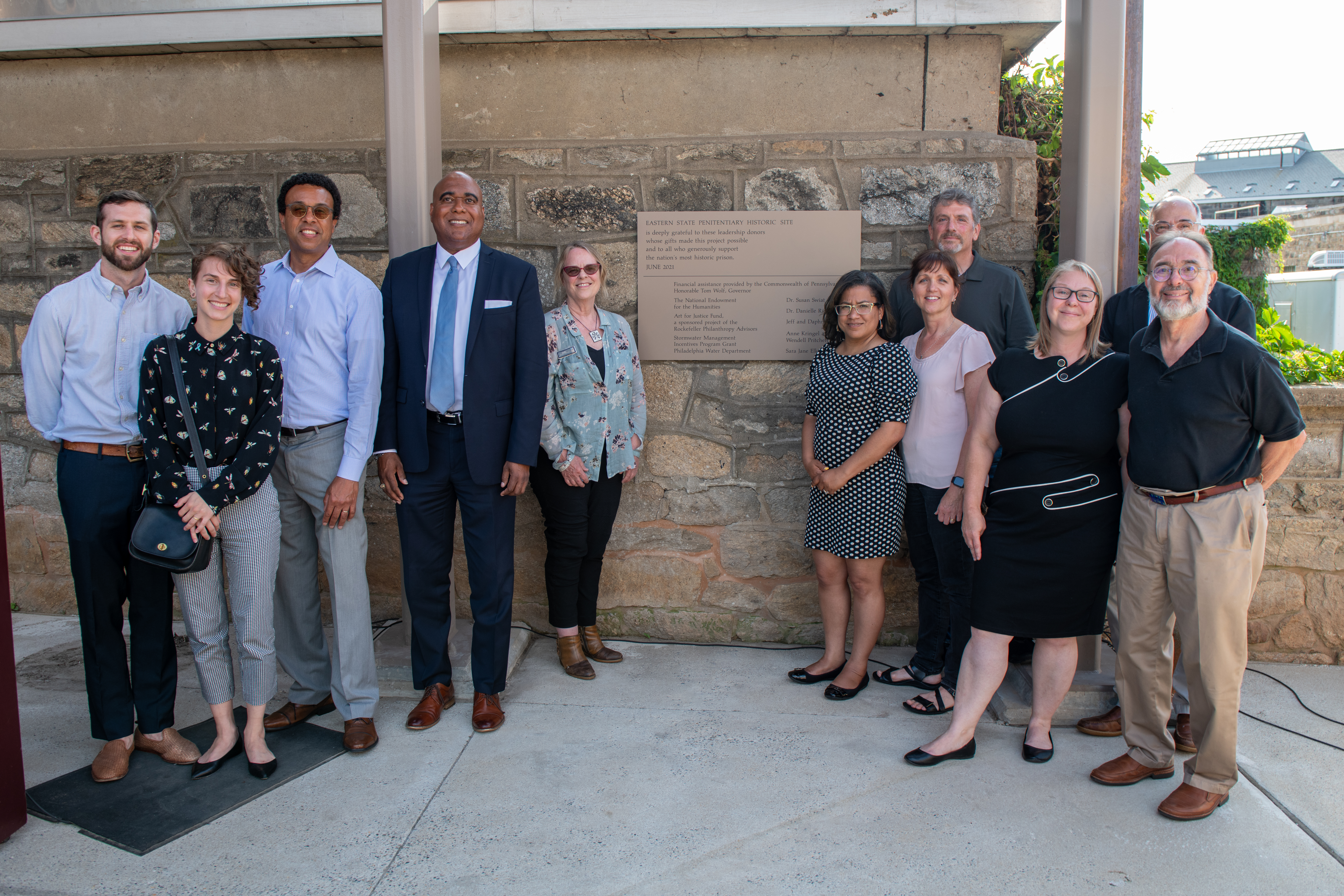 A photo of visitors at Eastern State Penitentiary. They are posing for a photo in front of a plaque.