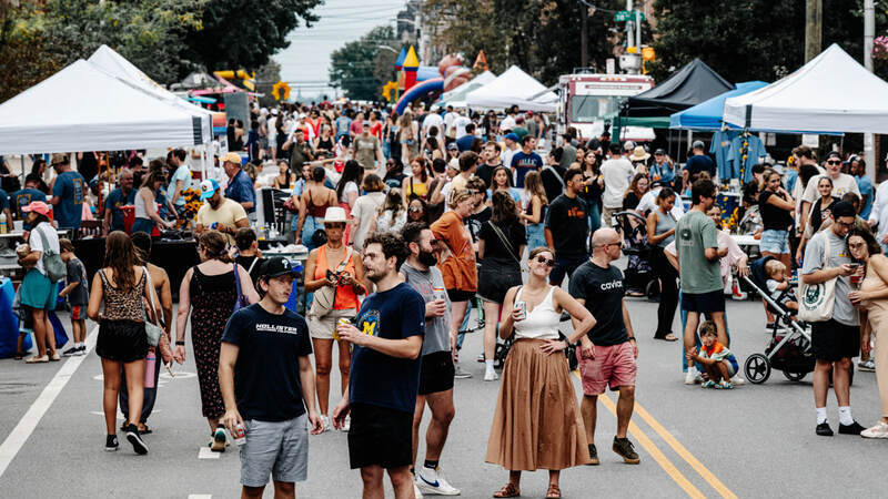 Crowded street scene at the Fairmount Sunflower Festival with vendor tents, visitors, and sunflowers displayed at market stalls.